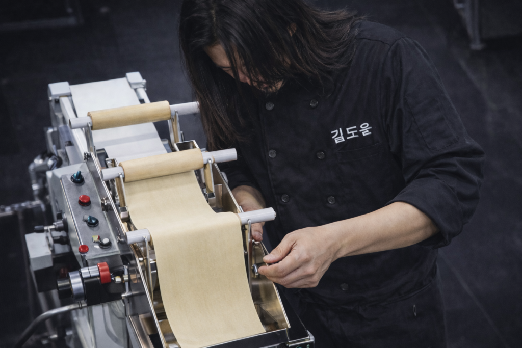 flat-noodle-sheet-being-rolled-through-pasta-machine